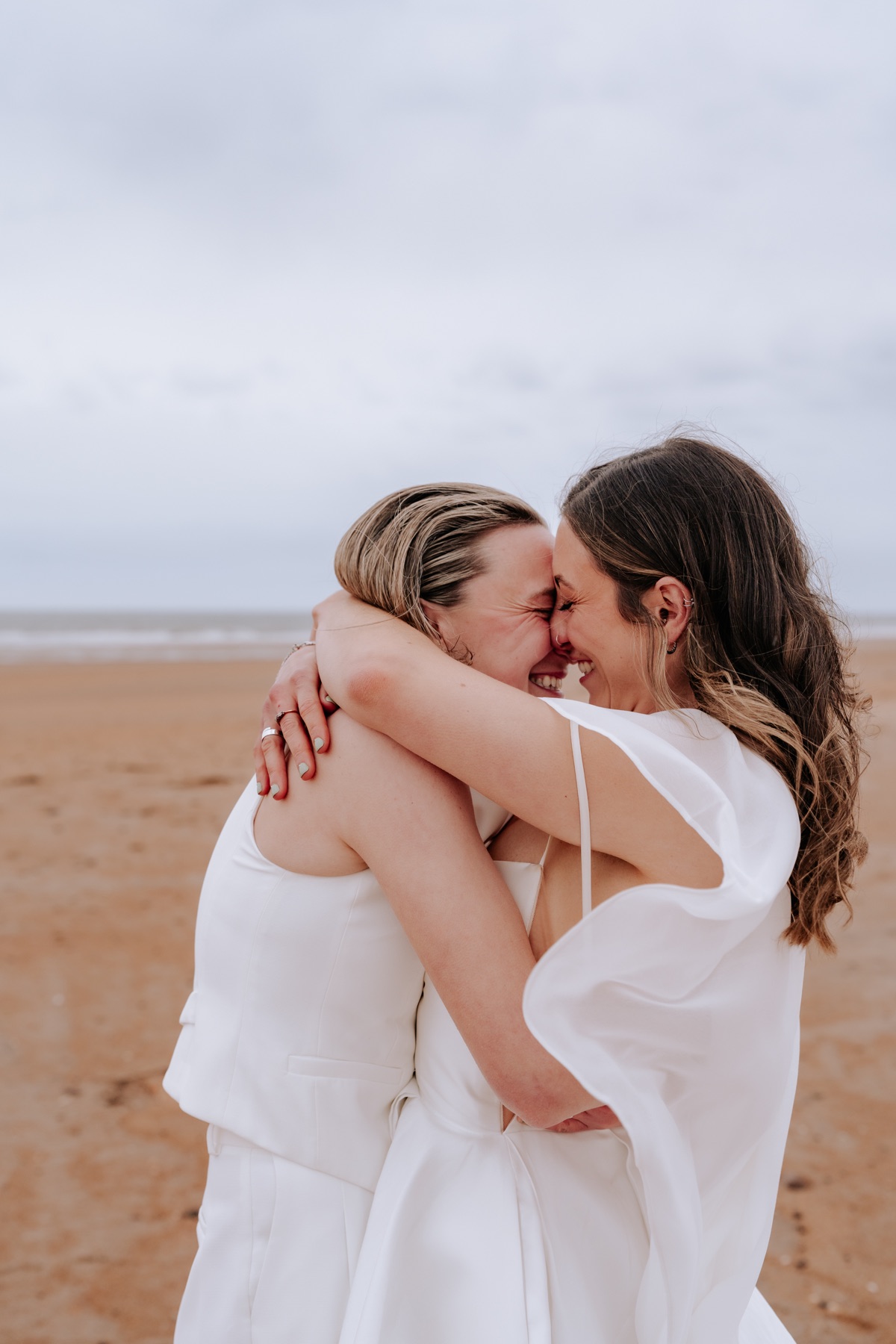 Hannah and Donna laughing together during their wedding portraits on the beach.