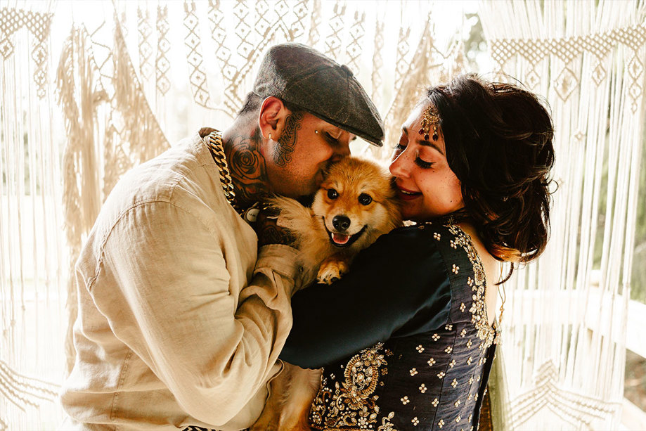 A man in a white shirt and a woman in a blue sari cuddle a small fluffy dog in between them