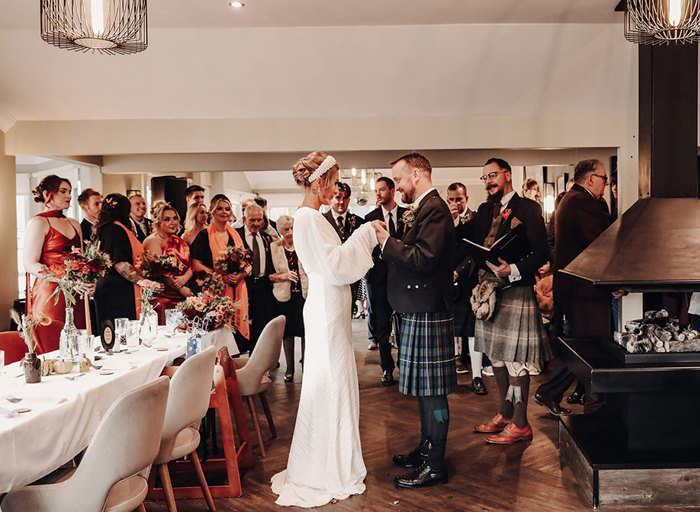 a bride and groom standing during a wedding ceremony as guests stand and look on in background