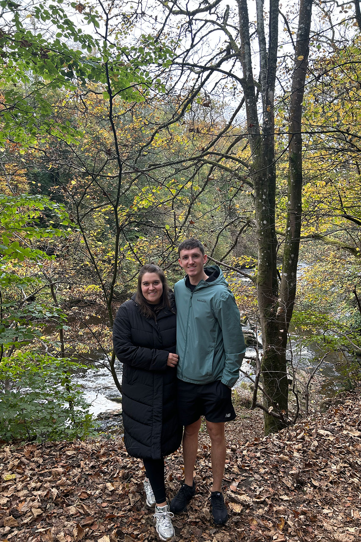 Bride-to-be and fiancé smiling together outdoors in a woodland setting