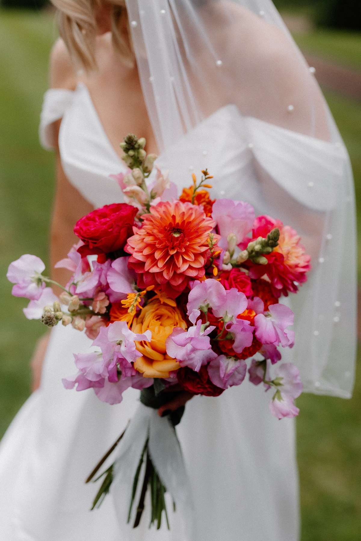 Close-up of Kara’s colourful pink, orange and red bridal bouquet by Pixie Rose Flowers at Prestonfield House.