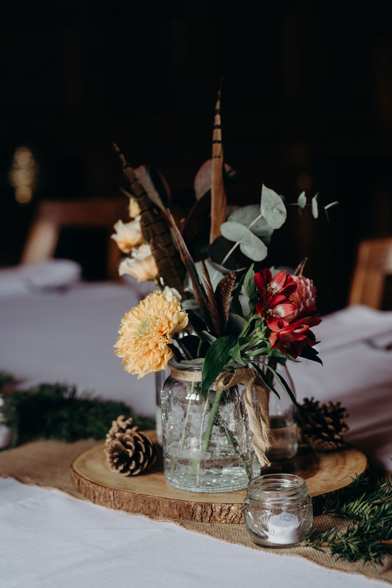 a small autumn wedding flower arrangement in a crackle glass jar sitting on a log slice