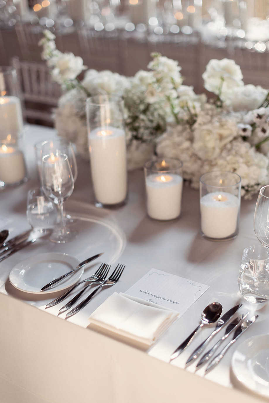  A table set for a wedding dinner party with wine glasses, white flowers and candles.