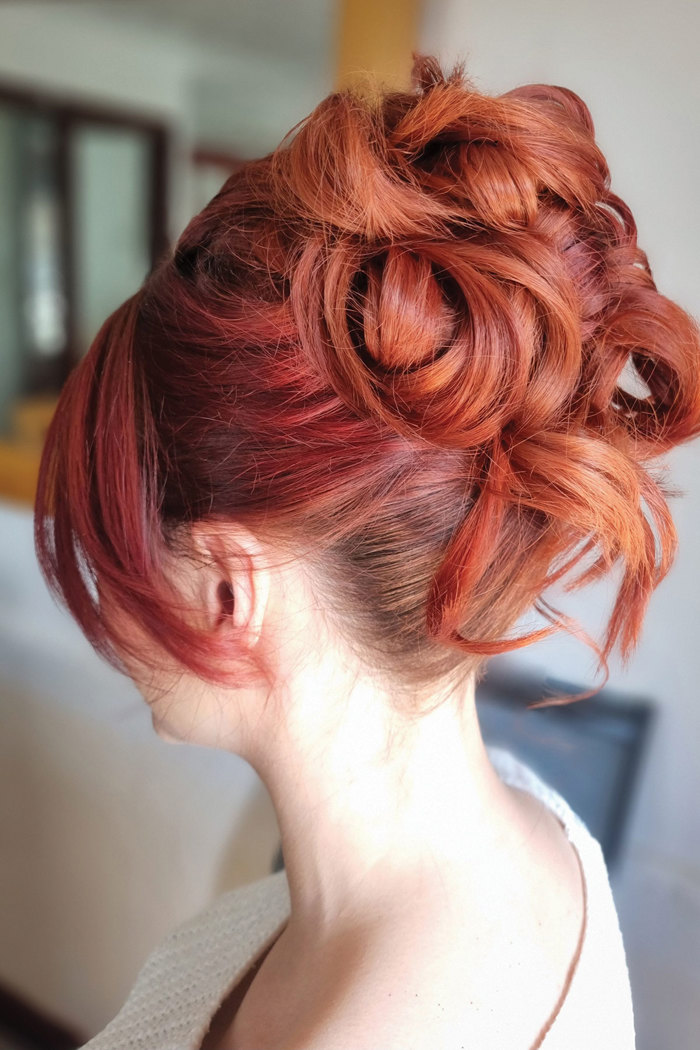 a close up photo of a woman with bright red hair styled up in an elaborate voluminous curly updo