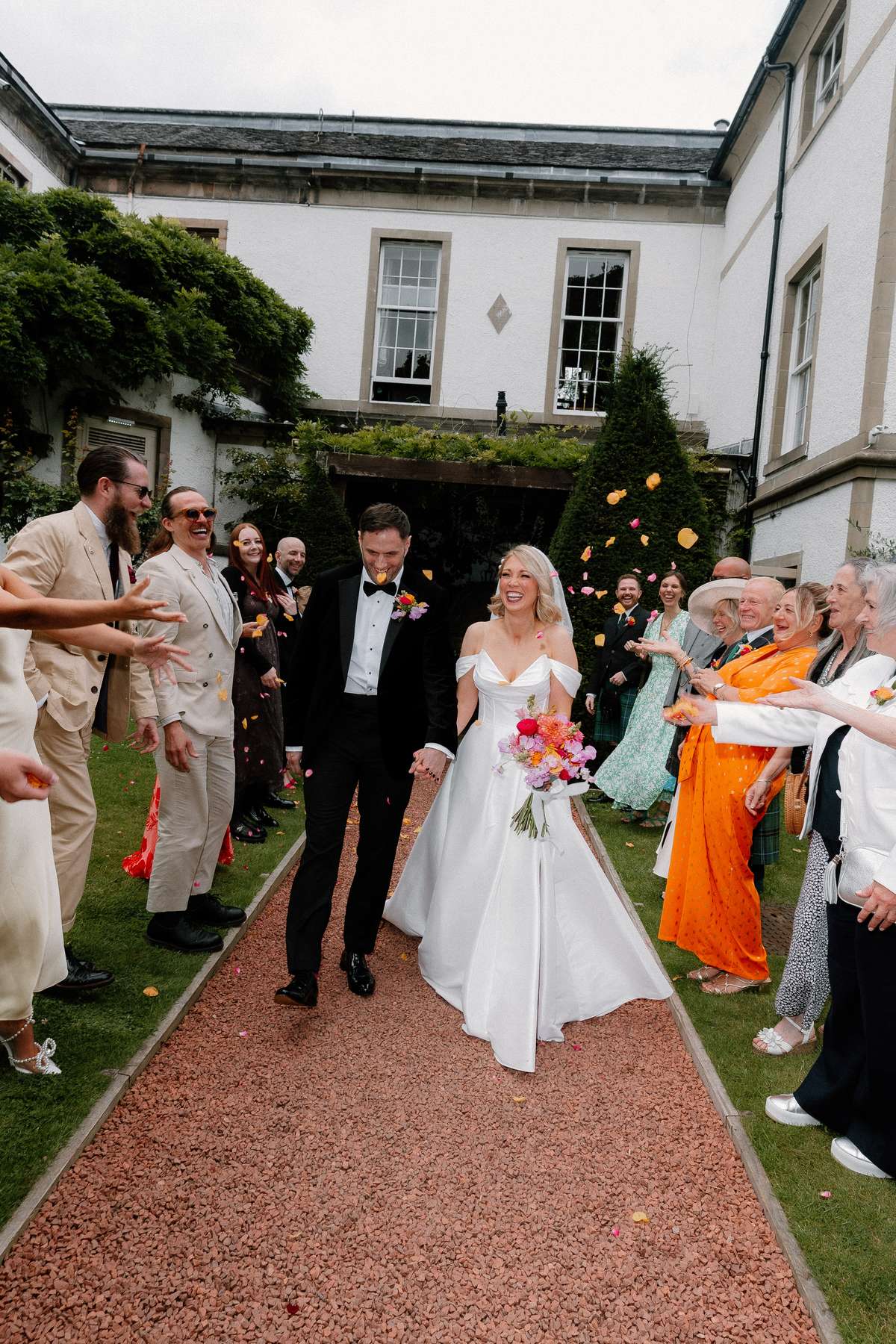 Kara and Rory walk through colourful confetti with their wedding guests at Prestonfield House in Edinburgh.