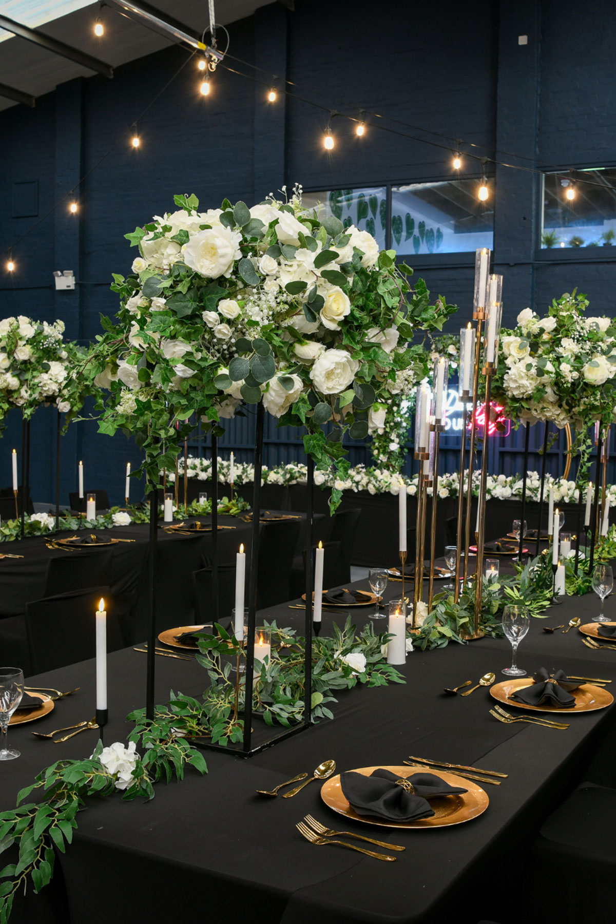 Black and gold wedding table setup at Geilsland Estate, with tall floral arrangements, candles and greenery.
