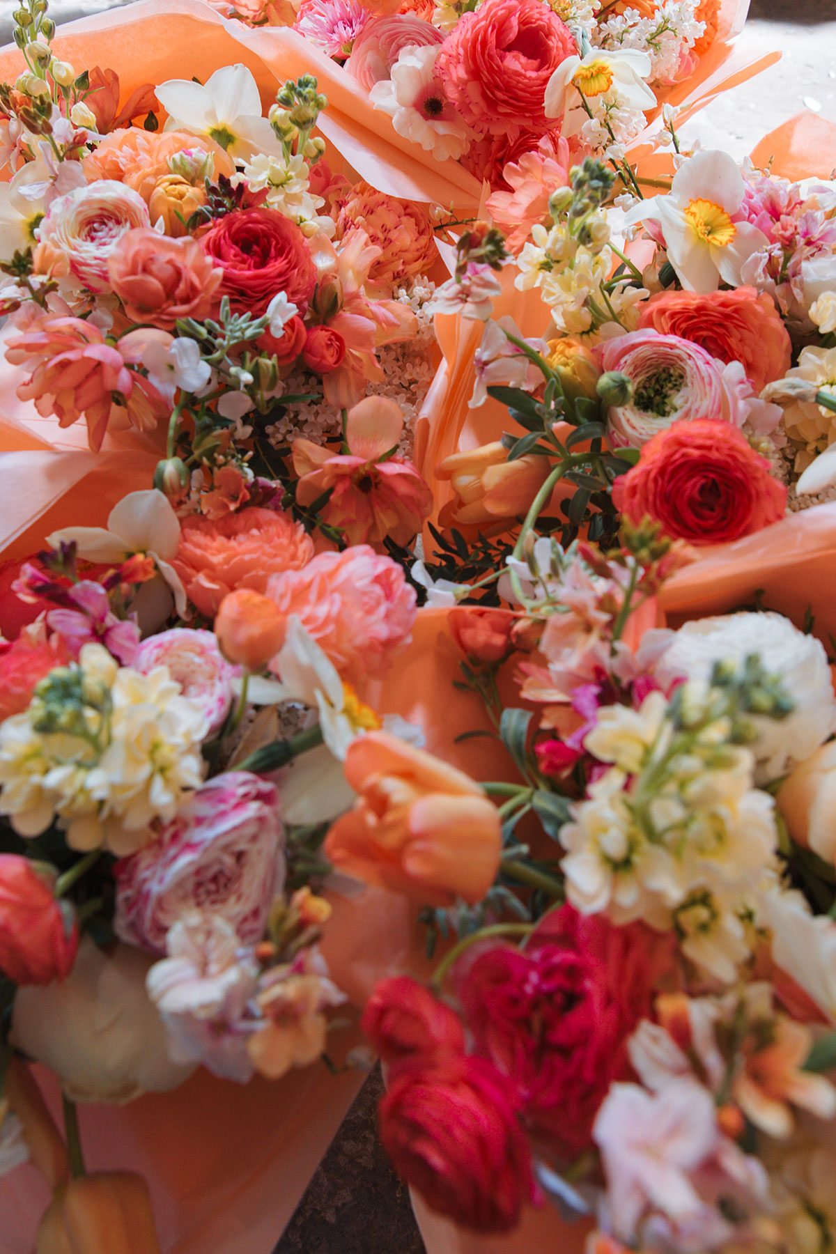 Colourful spring wedding bouquets with coral, peach and white flowers wrapped in orange paper