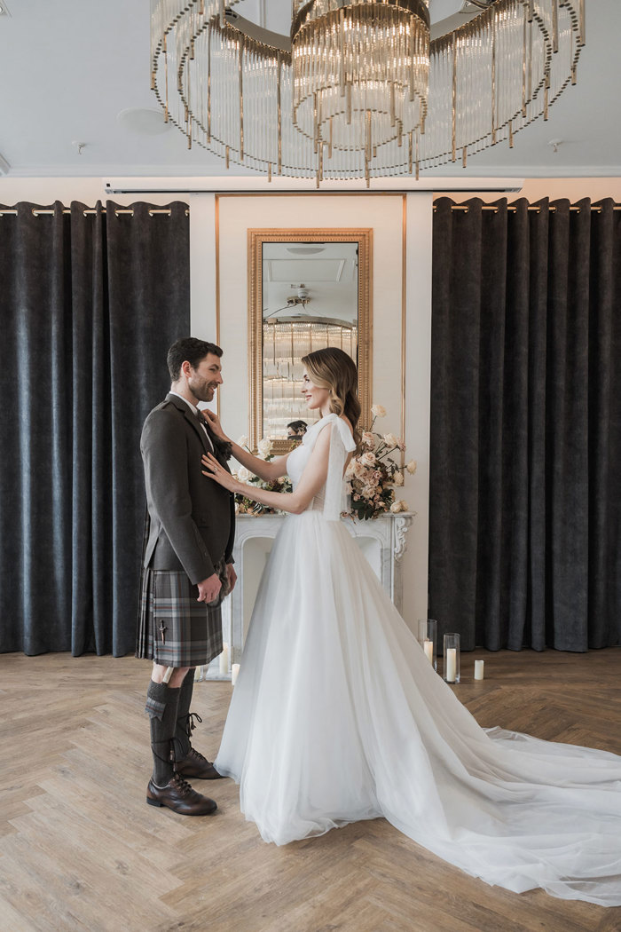a bride and groom standing on a wooden floor in front of a fireplace with mirror above it at The Exchange in Glasgow