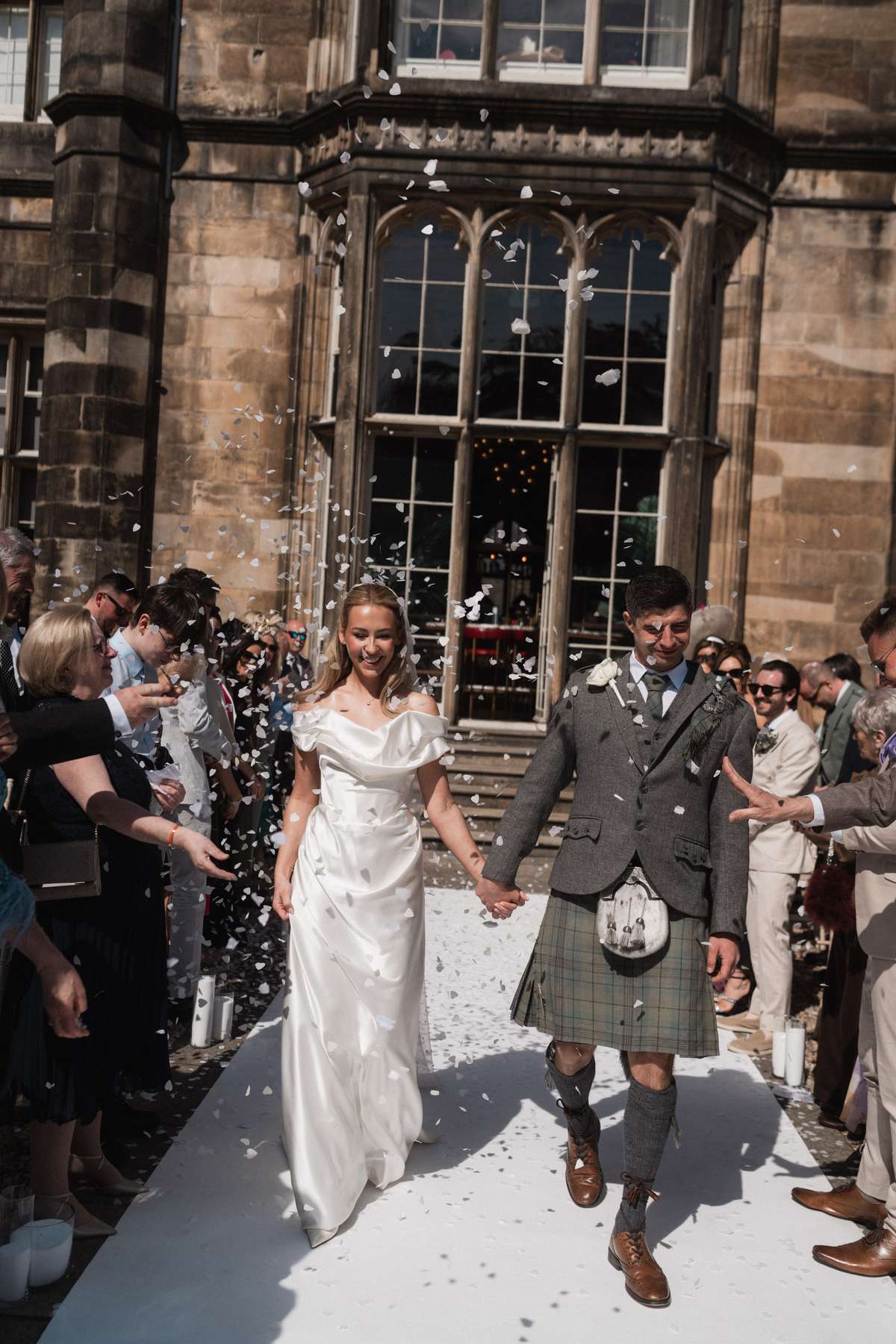 Newlyweds Siân and Stuart walk through a shower of white confetti outside Mar Hall following their spring wedding ceremony.