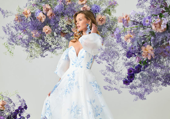 bridal model wears an off the shoulder puff sleeve gown covered in painted blue florals