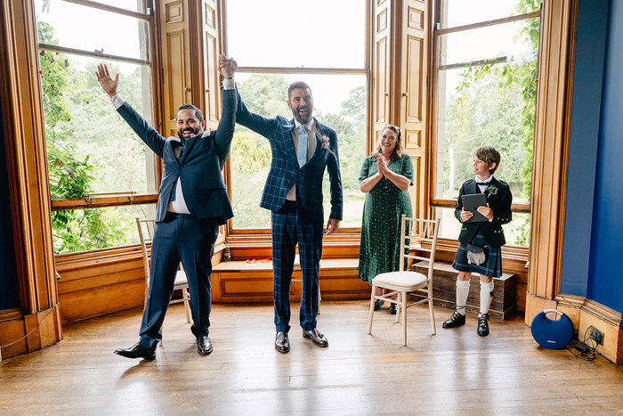 Grooms hold hands up triumphantly at the end of their wedding ceremony