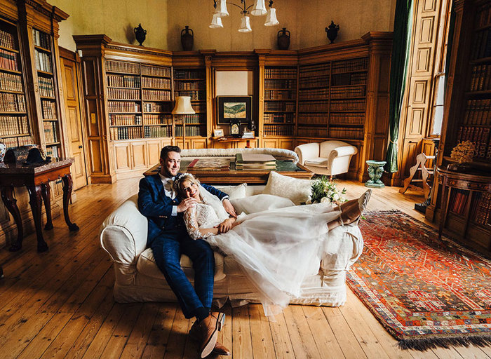 Bride and groom relax into each other on beige couch in an open library