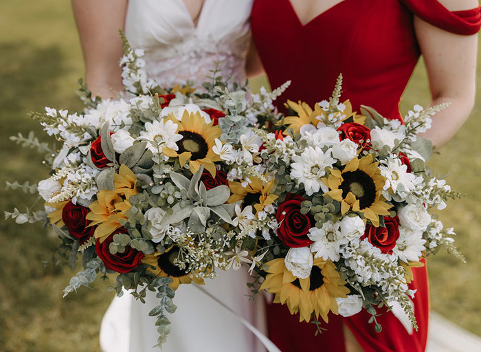 A close up of two bouquets with sunflowers, orange roses and white flowers