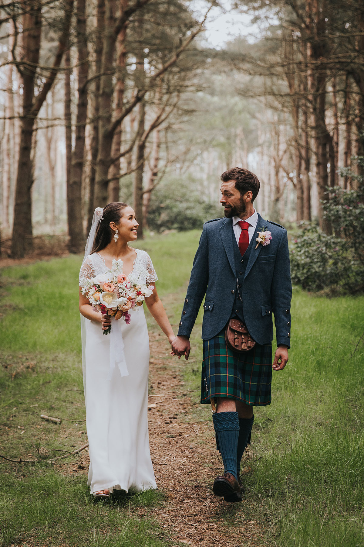 bride and groom walk towards the camera holding hands while wearing wedding outfits