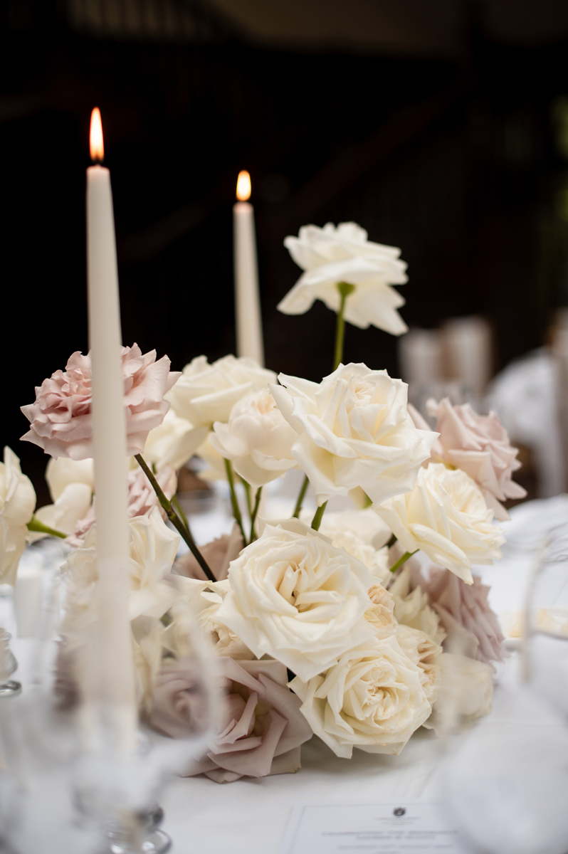 White and blush rose wedding centrepiece with lit taper candles decorating a reception table at Crossbasket Castle.