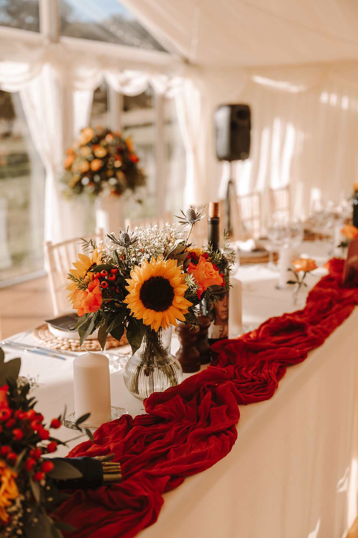 Close up shot of the table decor including a red runner, sunflowers and orange roses