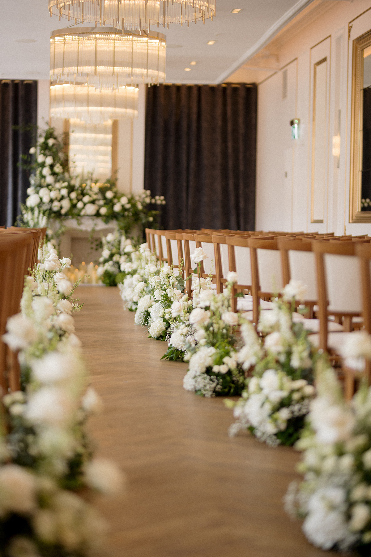 White floral aisle arrangements and chandeliers inside an elegant wedding ceremony room