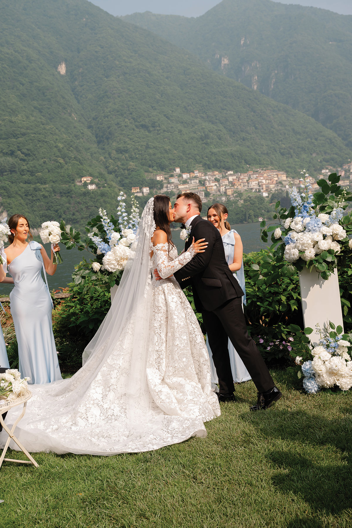 Bride and groom kissing during outdoor Lake Como wedding ceremony with mountain and lake views and blue and white florals