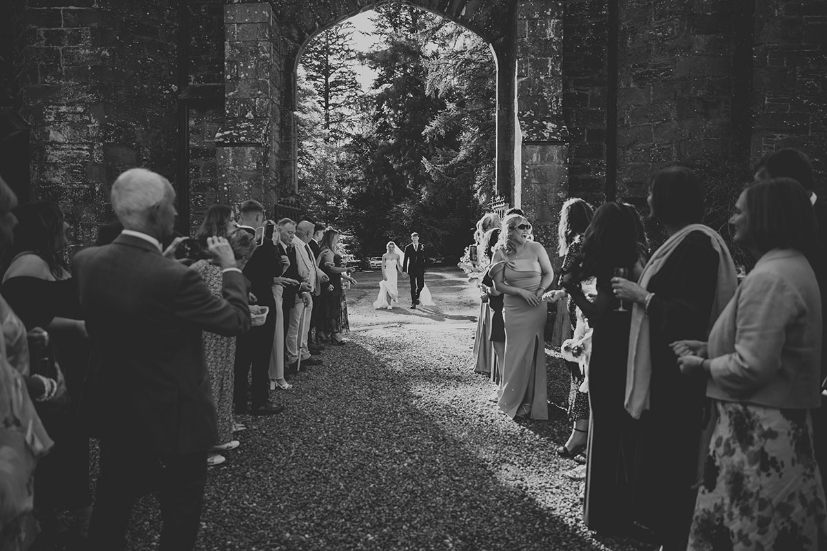 Black and white photo of guests lining archway for wedding confetti moment at estate entrance