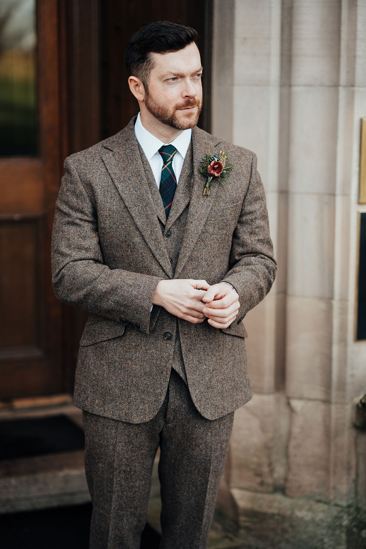 Groom in a brown tweed three-piece suit with tartan tie and seasonal buttonhole outside Schloss Roxburghe