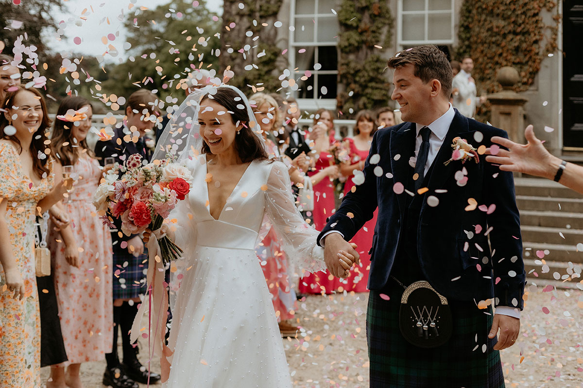 a bride and groom walking through a confetti shower outside Carlowrie Castle