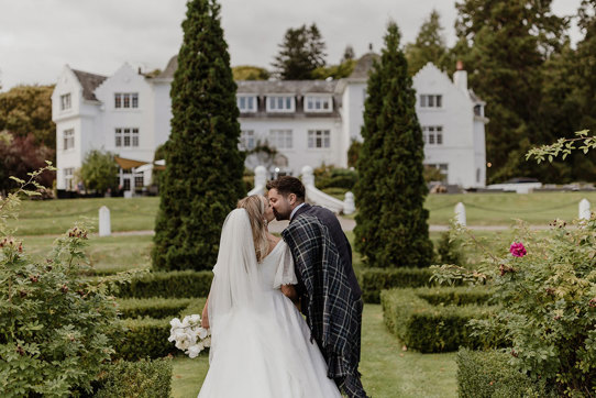 a bride and groom kissing in the garden at Achnagairn Castle