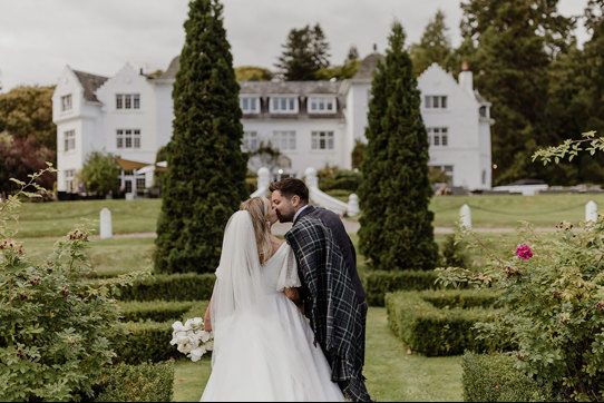 a bride and groom kissing in the garden at Achnagairn Castle