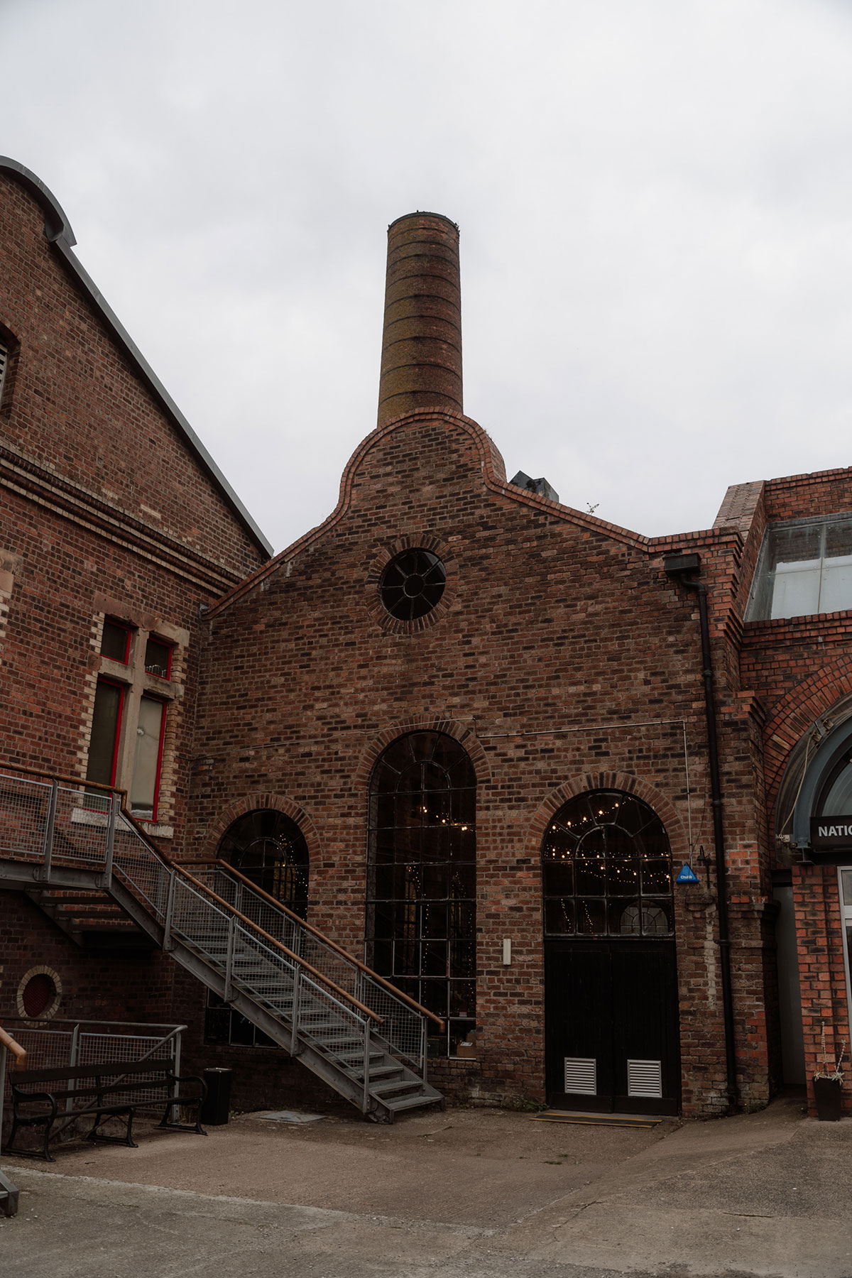 Exterior of a restored industrial wedding venue featuring red brick architecture, arched windows and a historic chimney stack