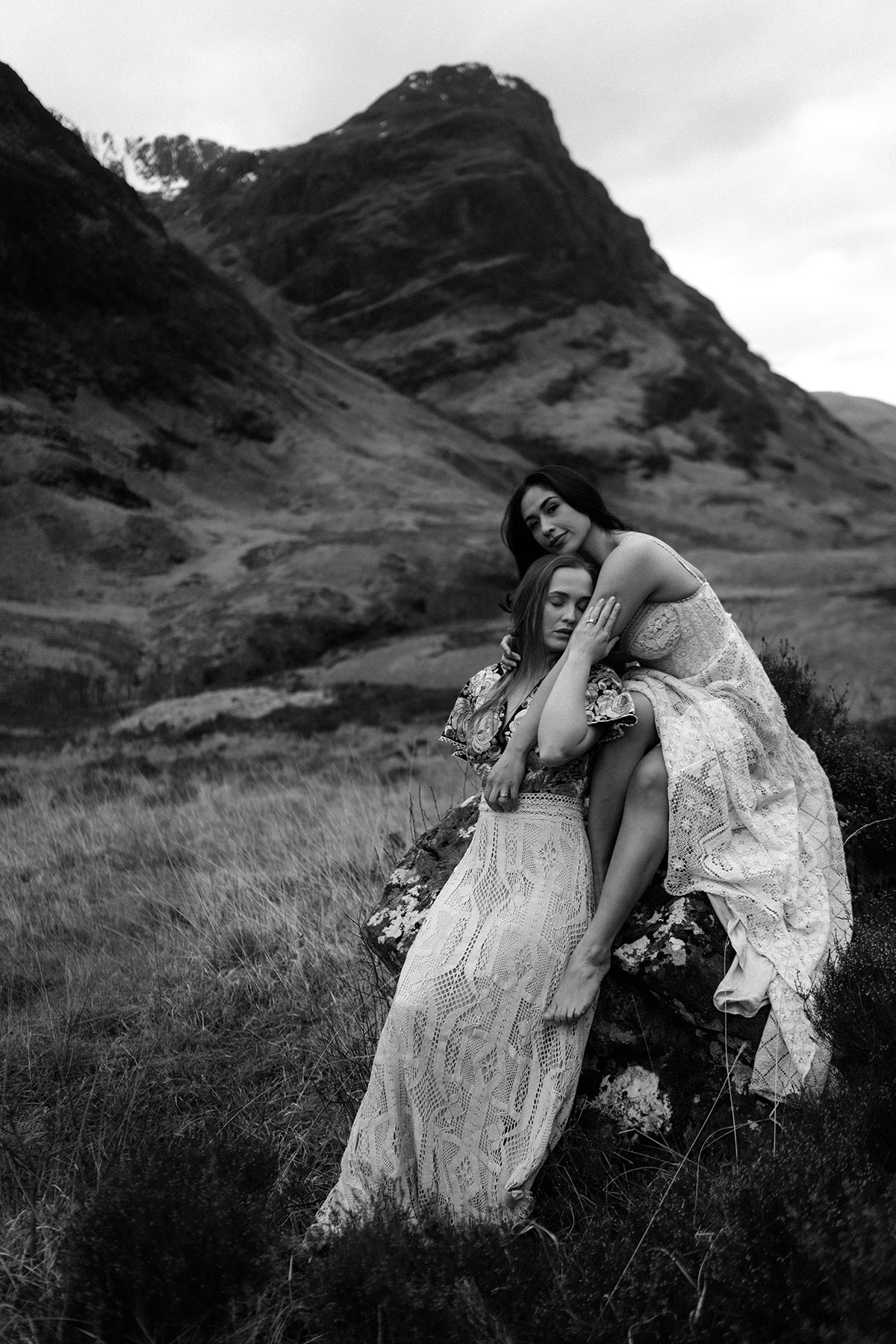 Black and white portrait of a couple in lace wedding dresses sitting on a rock during a Glencoe elopement shoot.