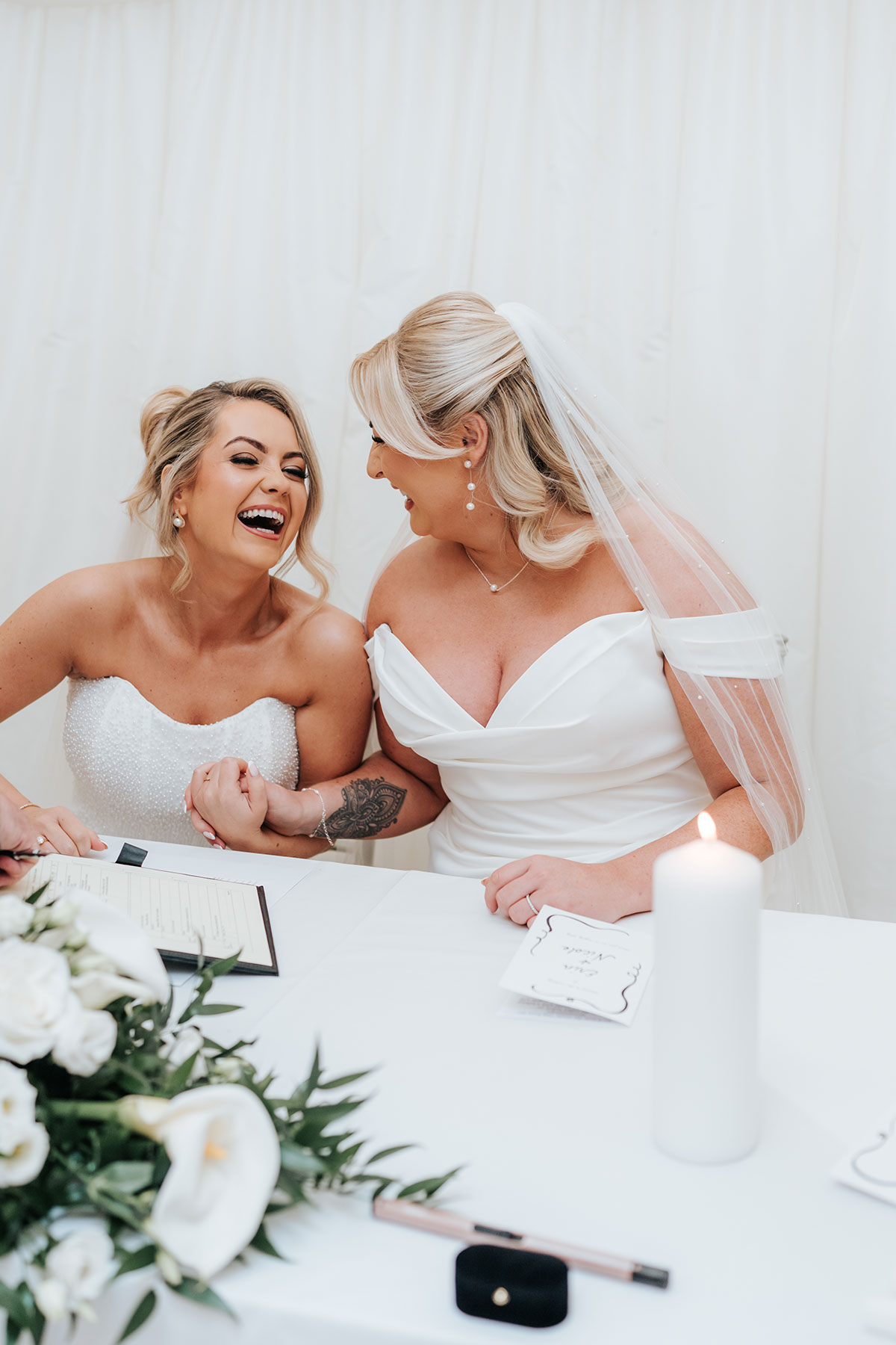 Newlywed brides laughing together as they sign their marriage paperwork during their Scottish wedding ceremony