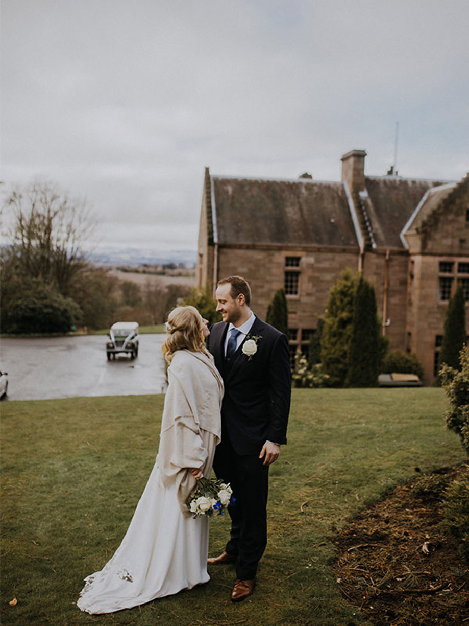 a bride and groom stand facing each other with a a country house and a green jeep in the background