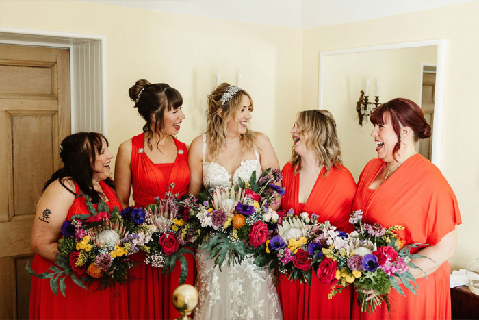 Bride and her bridesmaids who are dressed in red gowns all holding colourful bouquets 