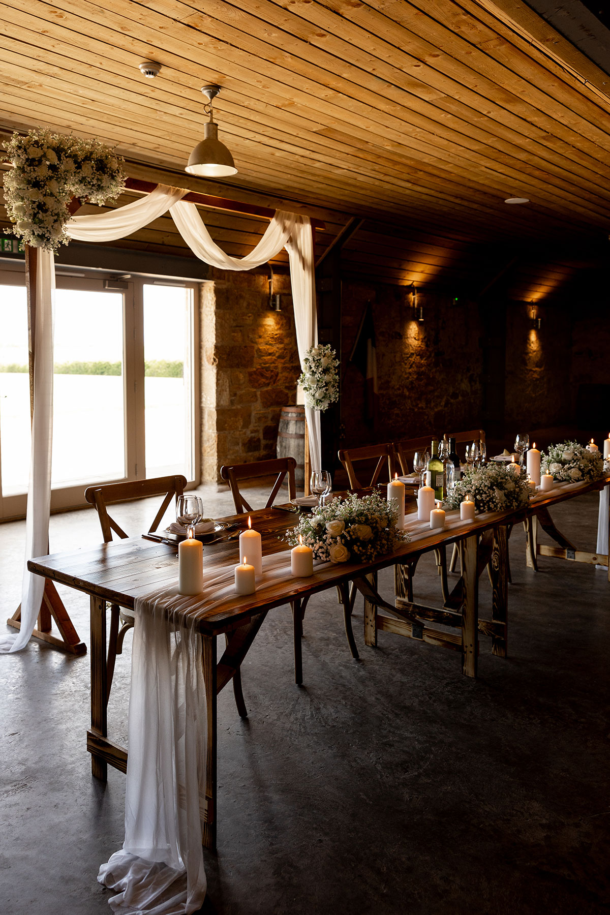 Top table at Falside Mill decorated with candles, draped fabric and white flowers in the softly lit barn venue.