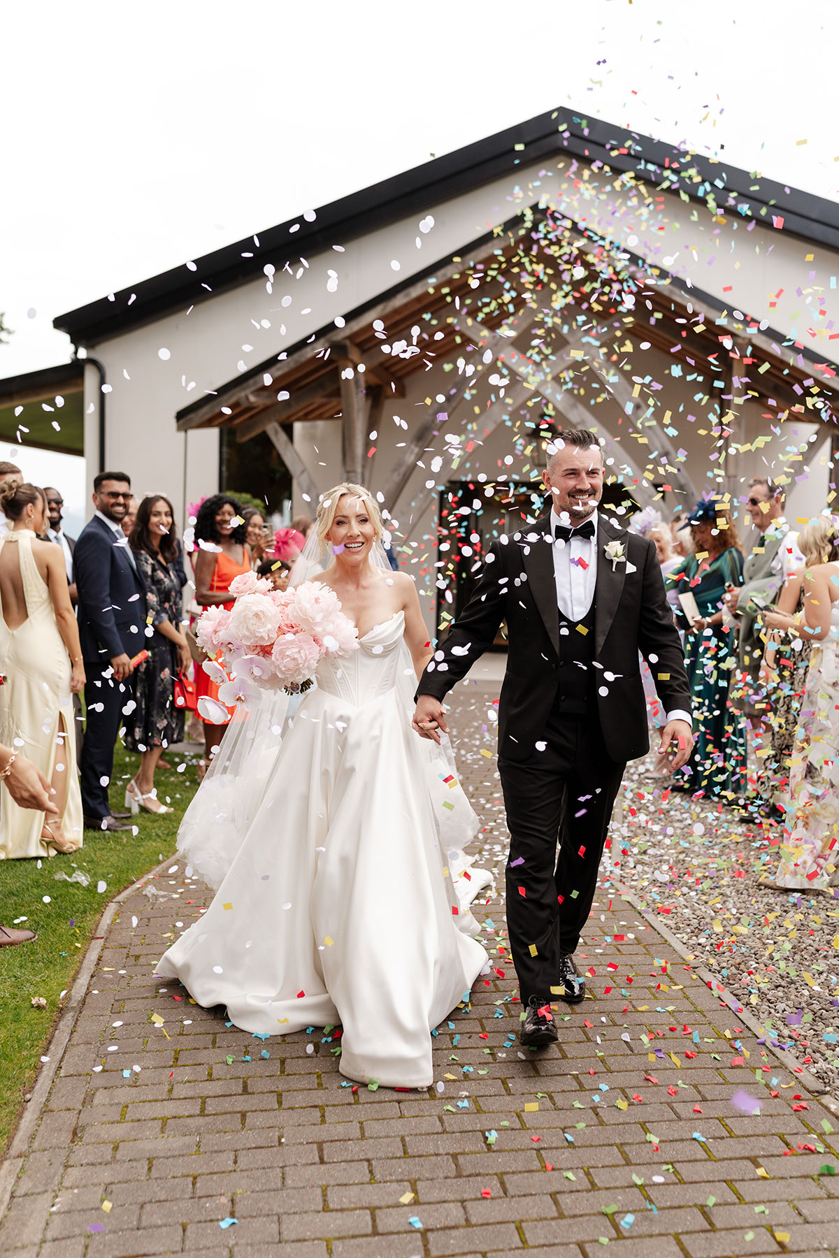 Bride and groom walk through colourful confetti after their Boturich Castle wedding ceremony surrounded by family and friends.