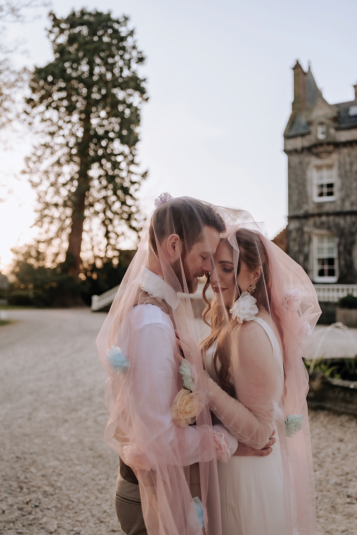 a bride and groom kissing under a pink veil at Carlowrie Castle