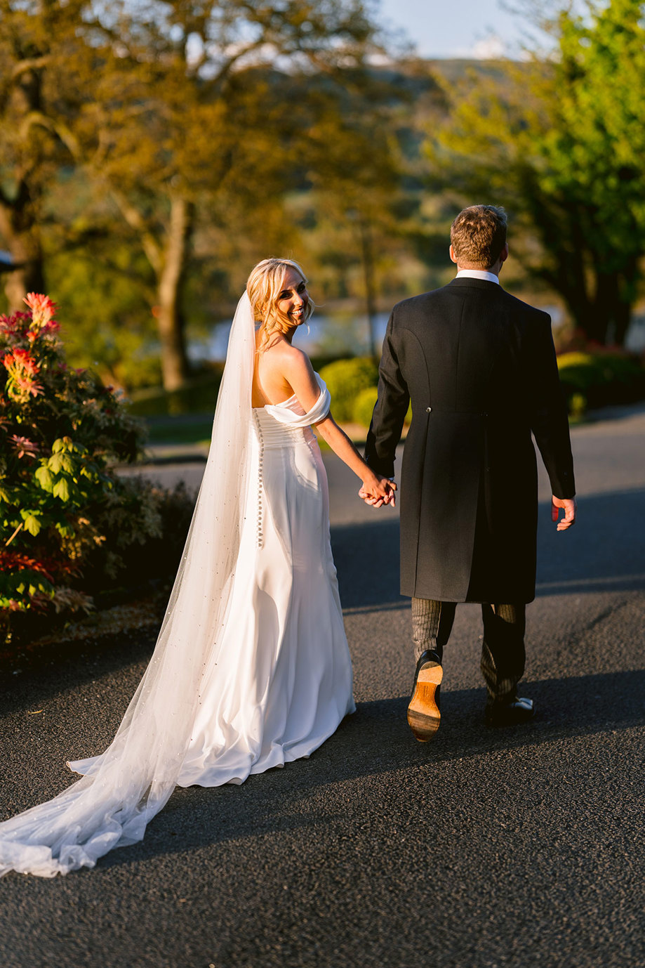 A bride and groom holding hands and walking down a road.