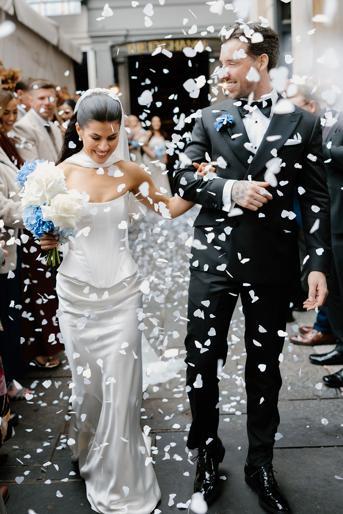 Newlyweds walking through white confetti outside The Exchange Glasgow wedding venue