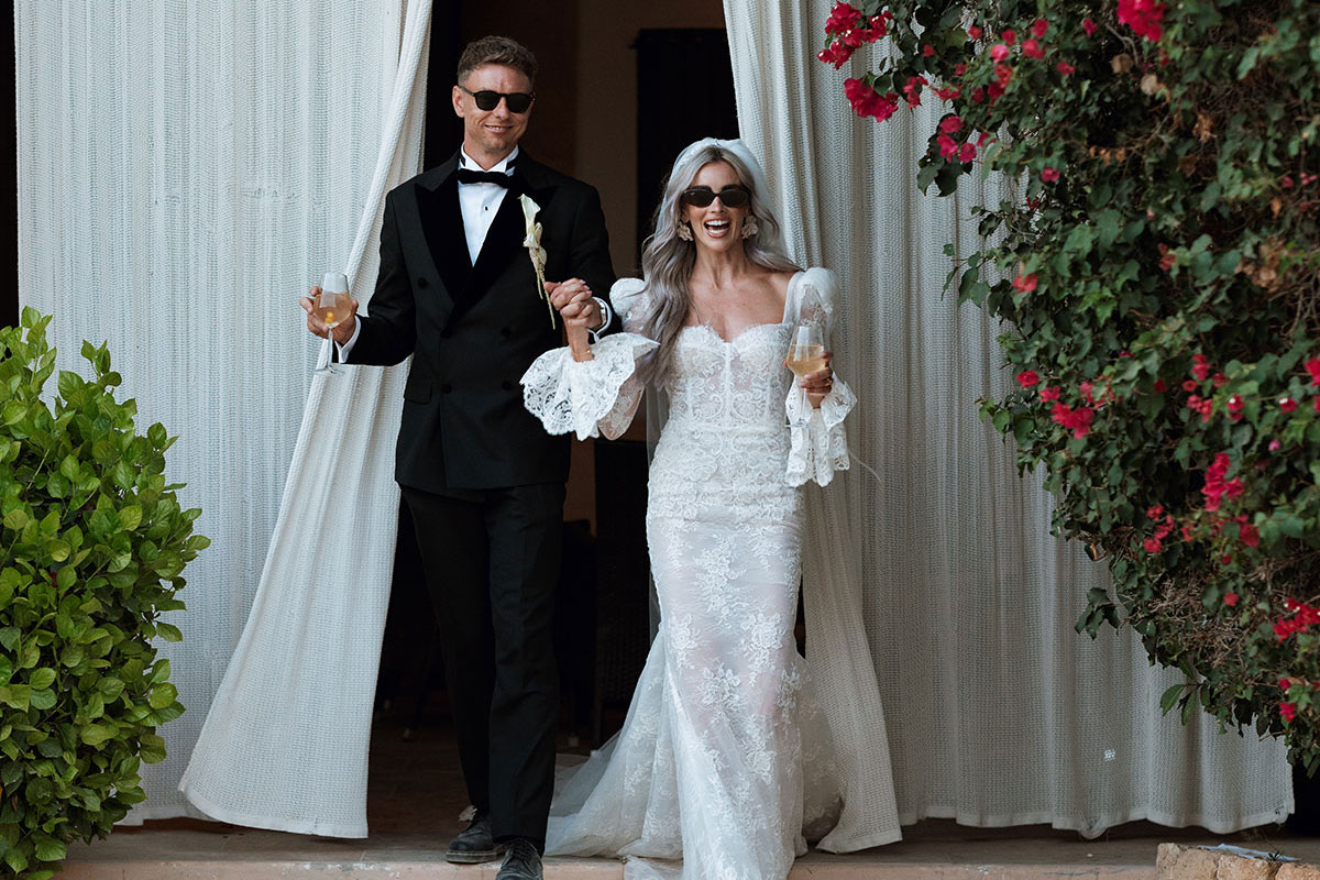Bride and groom emerging through white curtains with champagne glasses at Can Rafal Ibiza wedding reception