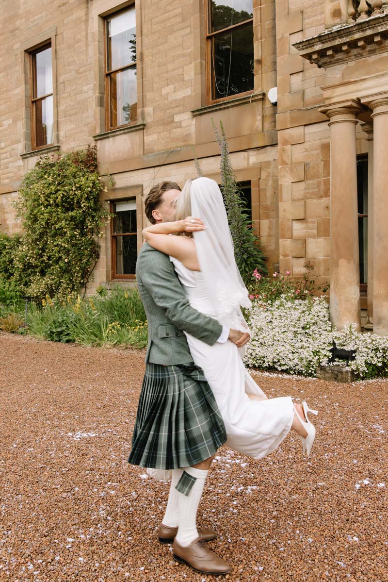 Louis lifts bride Lia as the newlyweds kiss outside Cambo House following their wedding ceremony.