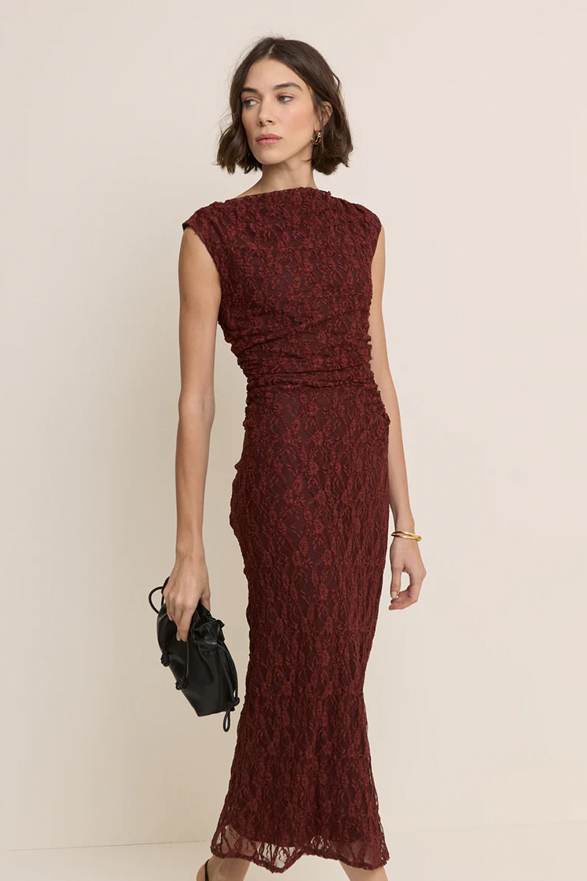 Woman wearing a burgundy lace maxi dress with a high neckline, ruched waist and sleeveless design.