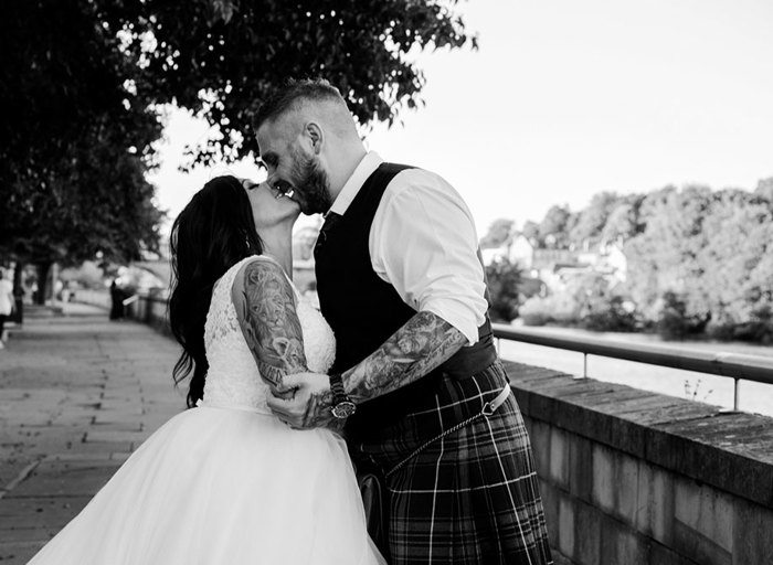 Black and white photo of a bride and groom kissing on a stone bridge