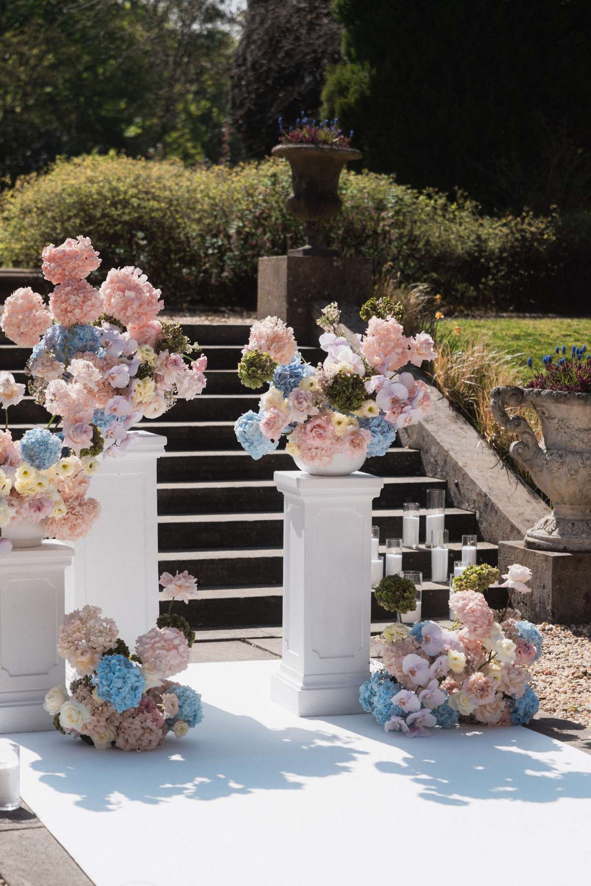 Pastel pink, blue and white wedding flowers arranged on white plinths for Siân and Stuart’s outdoor ceremony at Mar Hall.