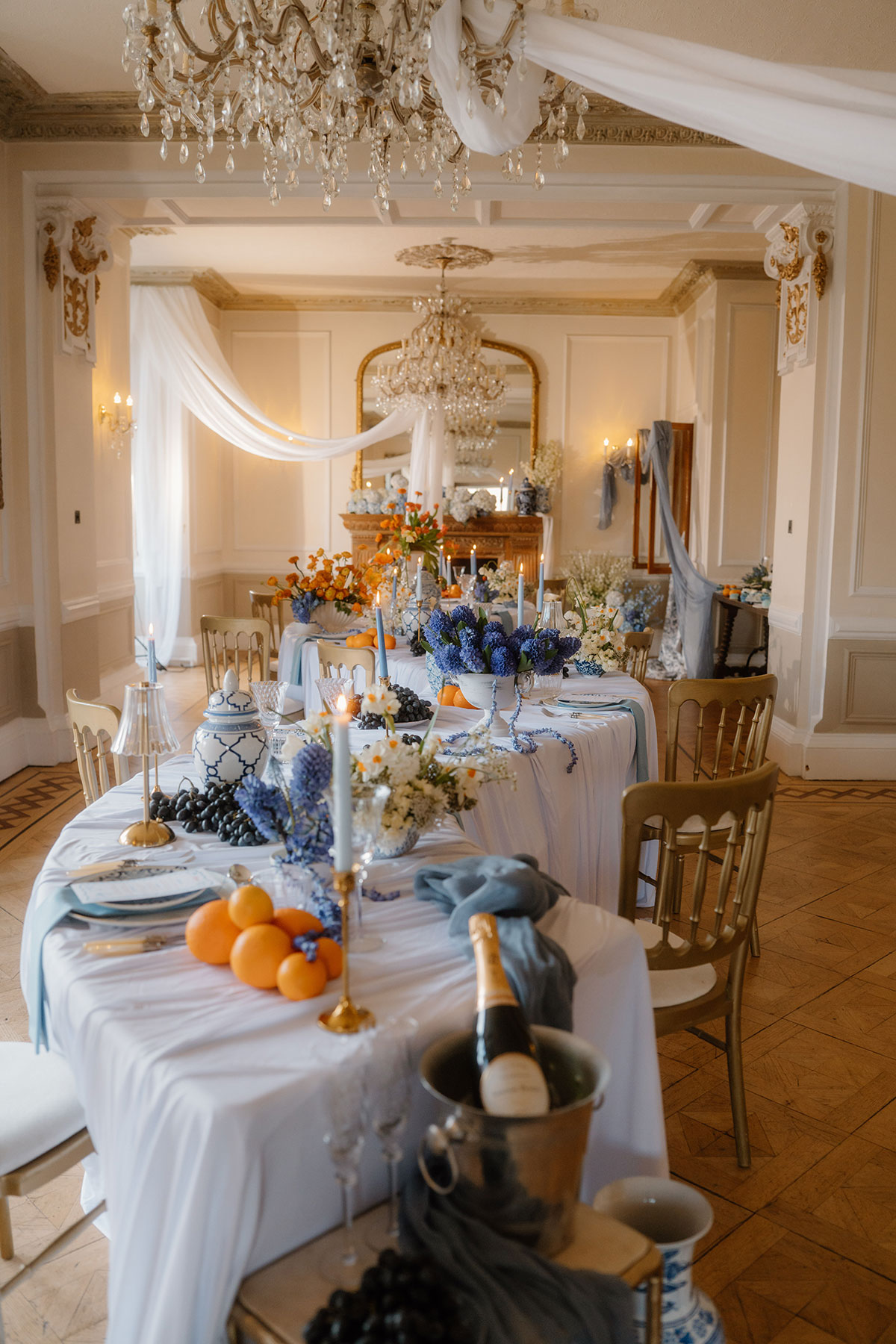Styled wedding breakfast setup at Auchen Castle featuring long banquet tables, crystal chandeliers, blue and white décor, fruit centrepieces and elegant place settings