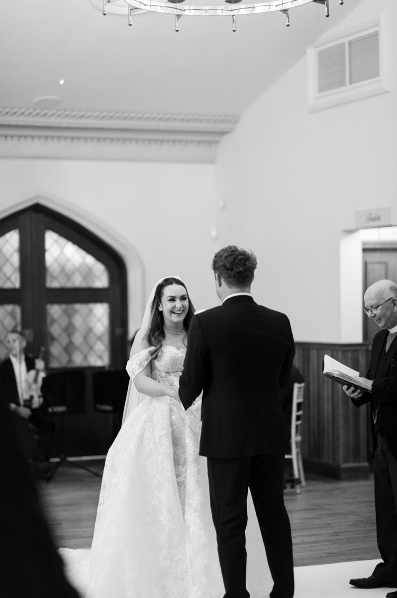 Bride and groom smiling at each other during their wedding ceremony in James Little Hall at Crossbasket Castle.