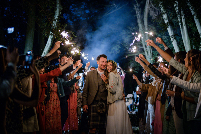 A Bride And Groom Surrounded By Guests Holding Sparklers At Nighttime At Raemoir House