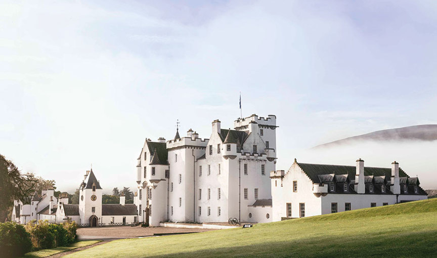 Exterior of Blair Castle with grass lawn in foreground and mist over hills in background