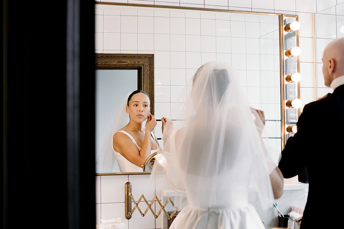 Bride adjusting earrings in mirror wearing veil before New York City Hall wedding ceremony