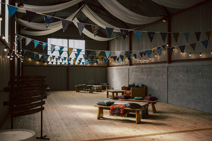 The inside of a stone barn with wooden benches, a wooden floor, blue bunting and fairylights 