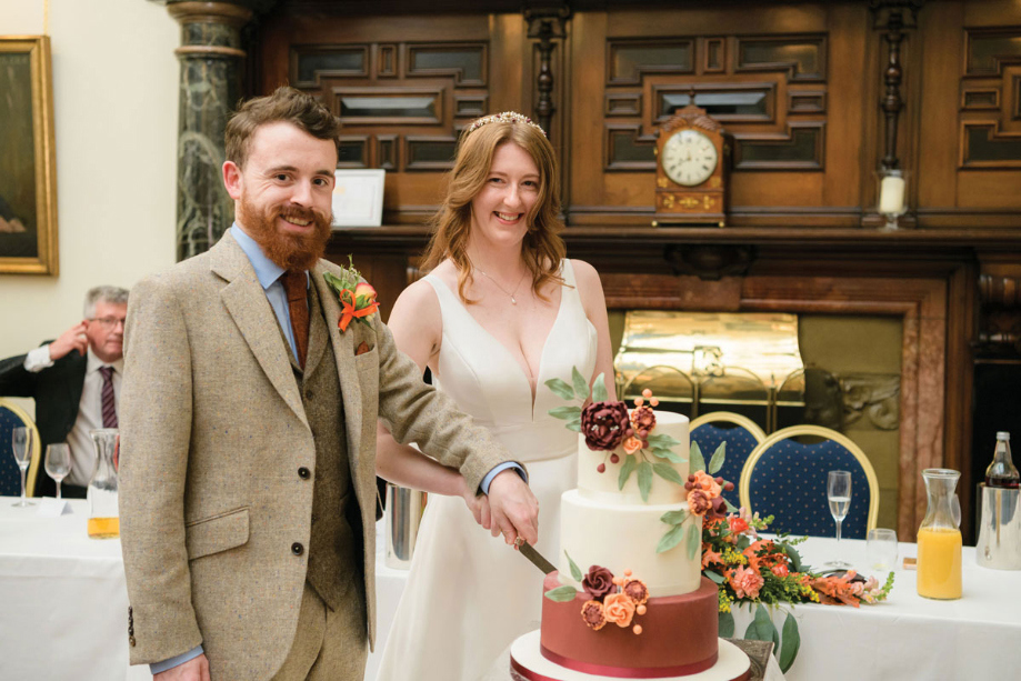 Bride and groom cut their wedding cake that is covered with autumnal foliage