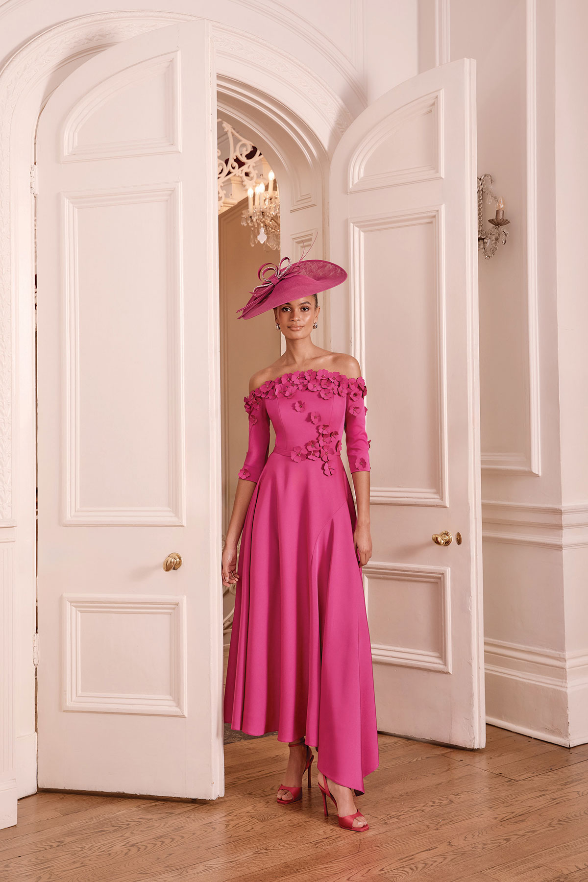 Pink off-the-shoulder mother of the bride dress with floral appliqué and matching statement hat.